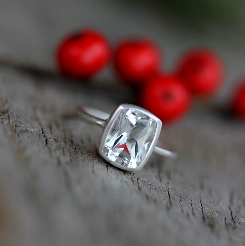 a handmade Cushion White Topaz Ring with a white topaz stone on top of red berries.