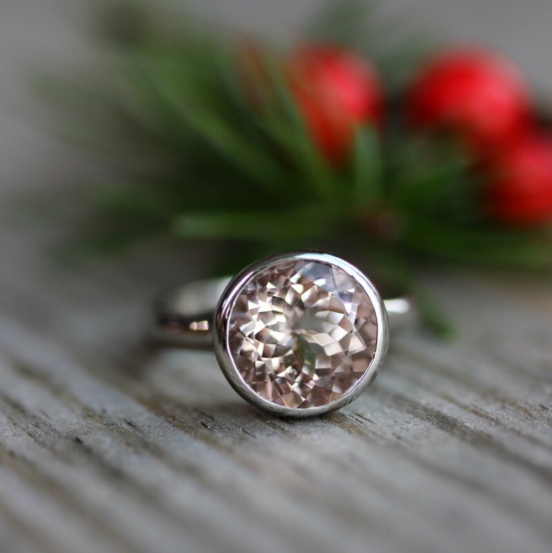 A Round Morganite Ring in White Gold sitting on a wooden table, handmade by Cassin Jewelry.