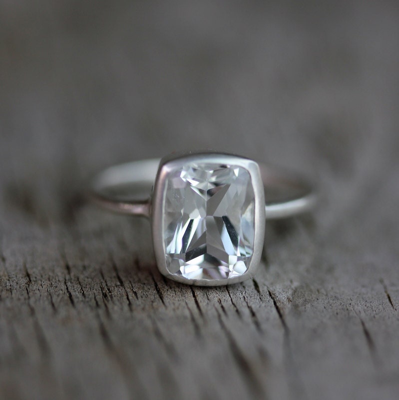A Handmade Cushion White Topaz Ring on a wooden surface.