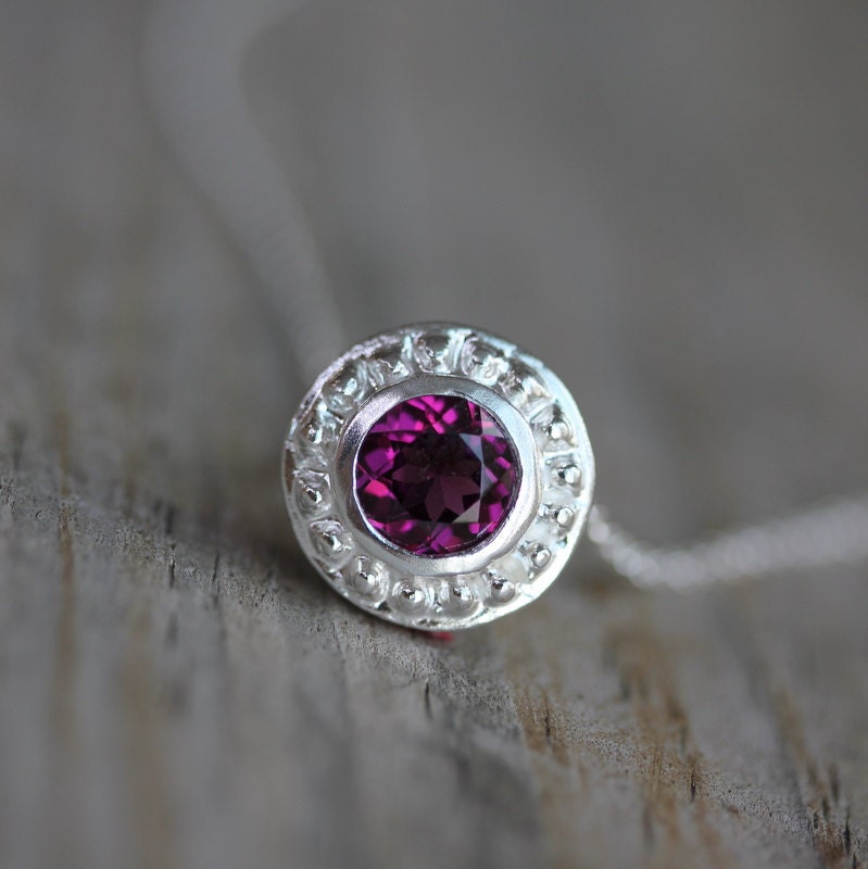 Handmade Pink Rhodolite Garnet Slide Necklace with a purple stone on top of a wooden table.