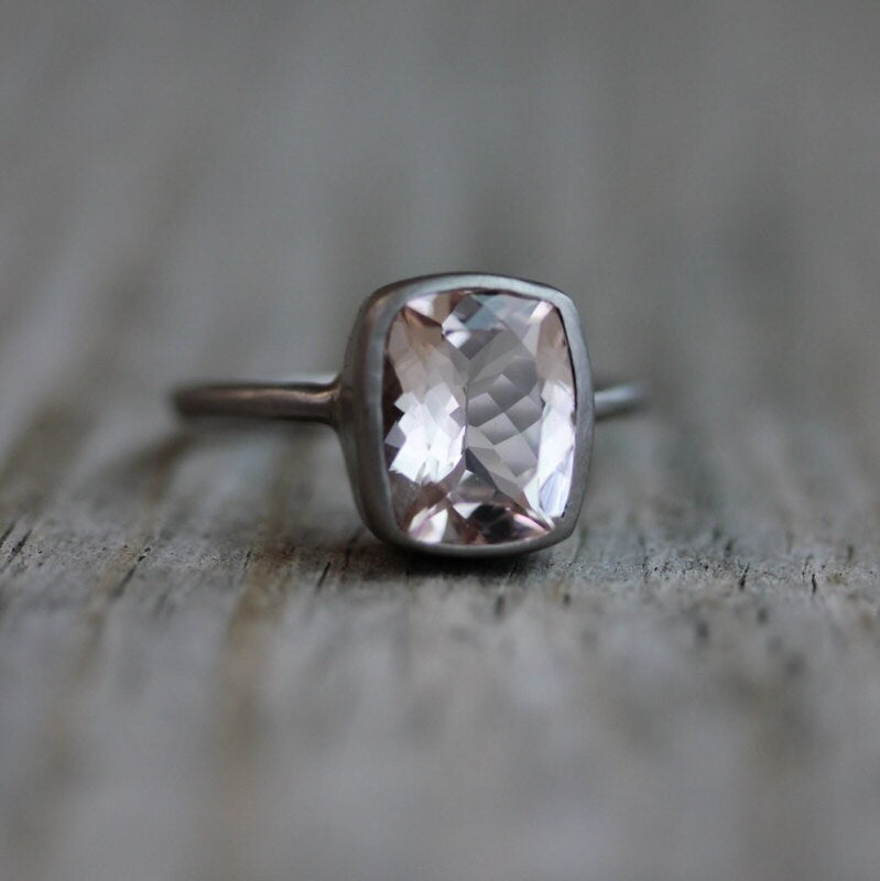 A Handmade Morganite Ring in Palladium White Gold sitting on top of a wooden table.
