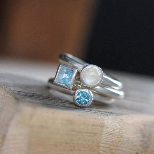 Handmade jewelry featuring a stack of Rainbow Moonstone Rings with blue topaz and aquamarine stones.