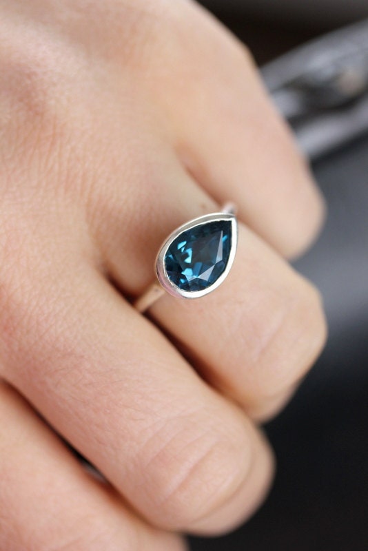 A woman's hand holding a handmade Large London Blue Topaz Sideswept Ring.
