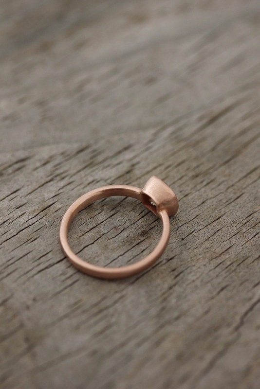 A Handmade Cushion Cut Rose Gold Engagement Ring showcased on a wooden table.