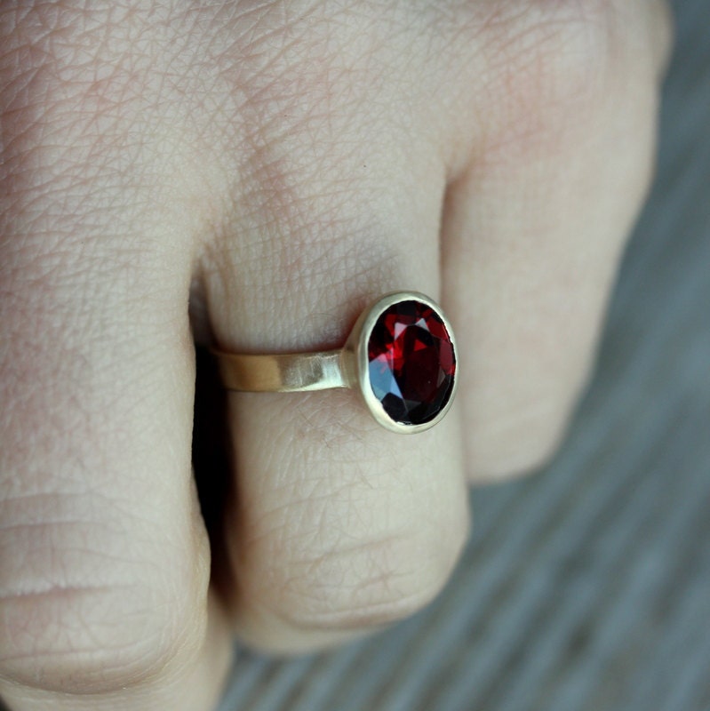 A person wearing a handmade Oval Red Garnet Ring in 14k Yellow Gold Bezel Setting.