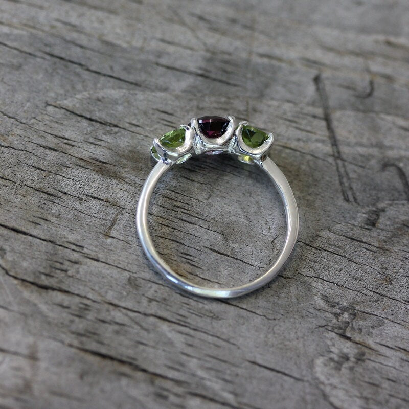 A Raspberry Rhodolite Garnet Three Stone Ring with peridots and emeralds, handmade by Cassin Jewelry.