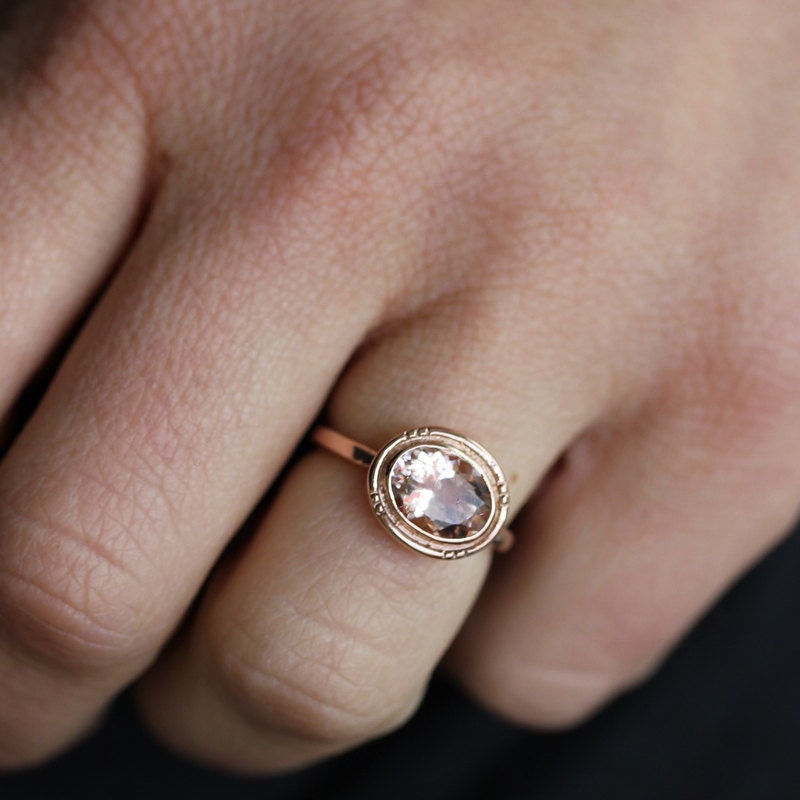 A woman's hand holding a handmade Oval Morganite Ring with Halo Design by Cassin Jewelry.