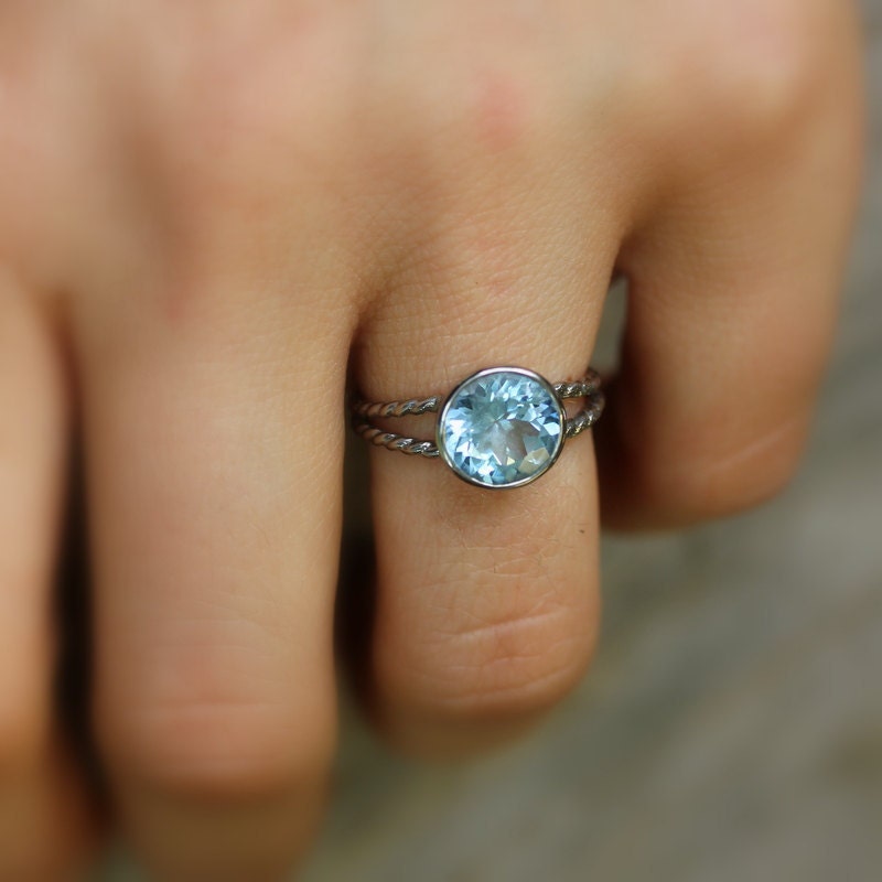 A woman's hand is holding a handmade Round Aquamarine Split Shank Setting in Sterling Silver by Cassin Jewelry.