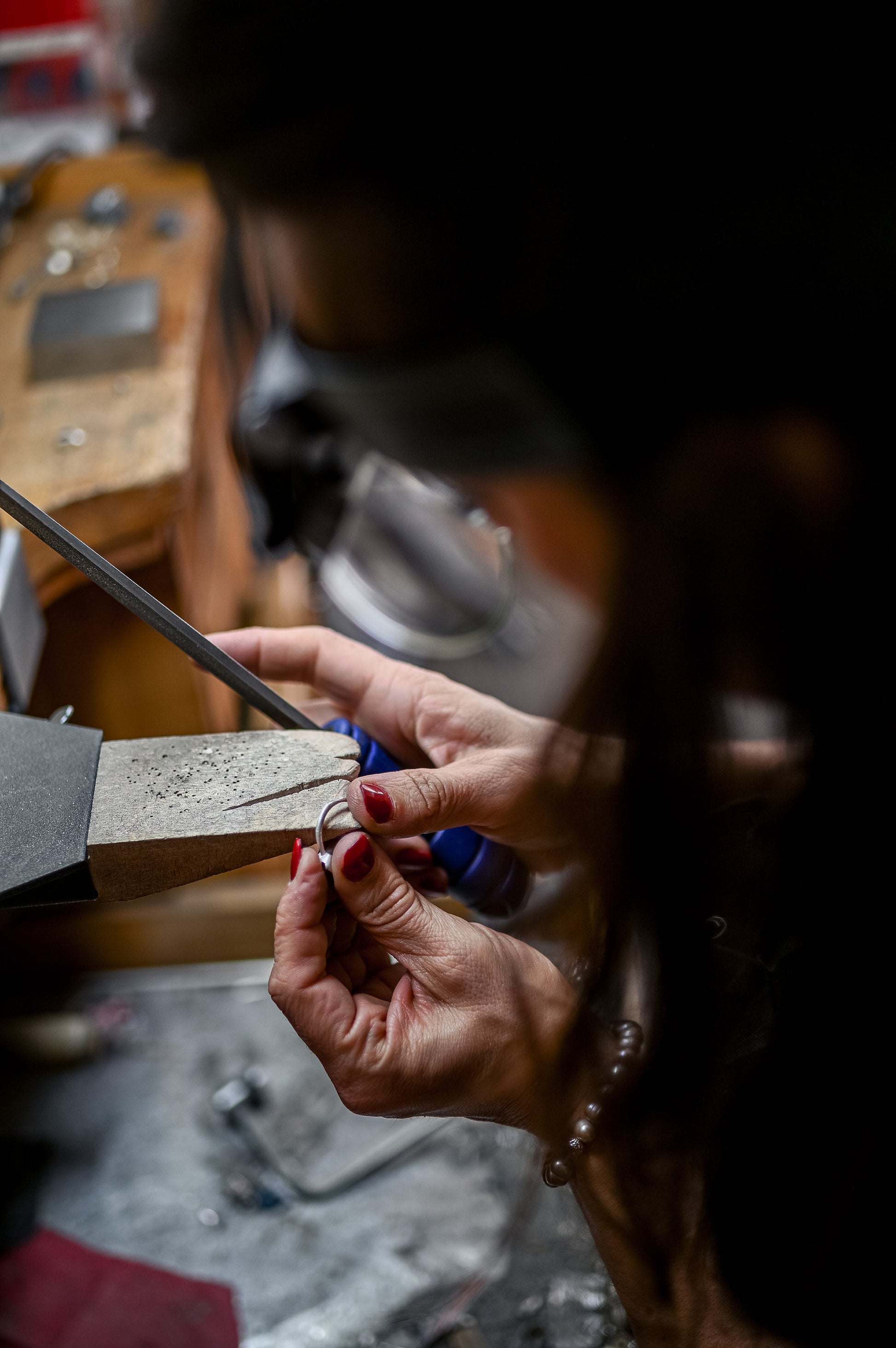 A woman is working on the Oregon Sunstone Milgrain Ring in Brushed Sterling Silver, creating exquisite handmade jewelry for Cassin Jewelry.