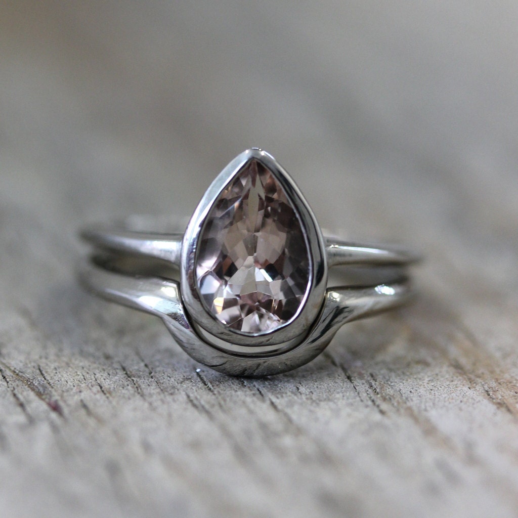 A Handmade Pear Shaped Morganite Ring in White Gold on a wooden surface.