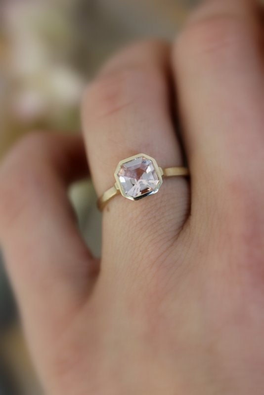 A woman's hand holding a handmade Asscher Cut Morganite Ring in 14k yellow Gold by Cassin Jewelry.