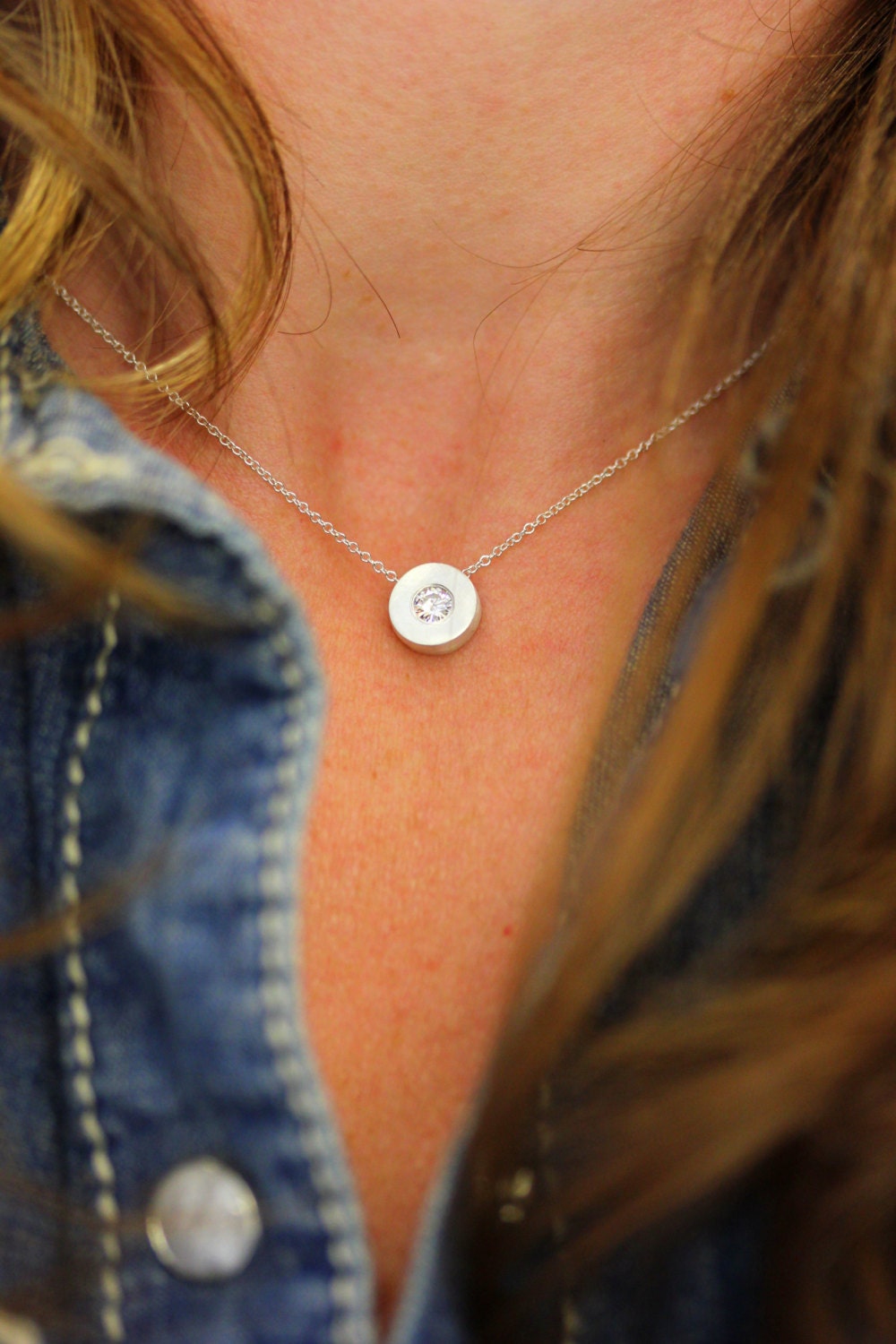 A close-up of a woman wearing handmade jewelry, the Moissanite and Sterling Silver Slide Pendant.