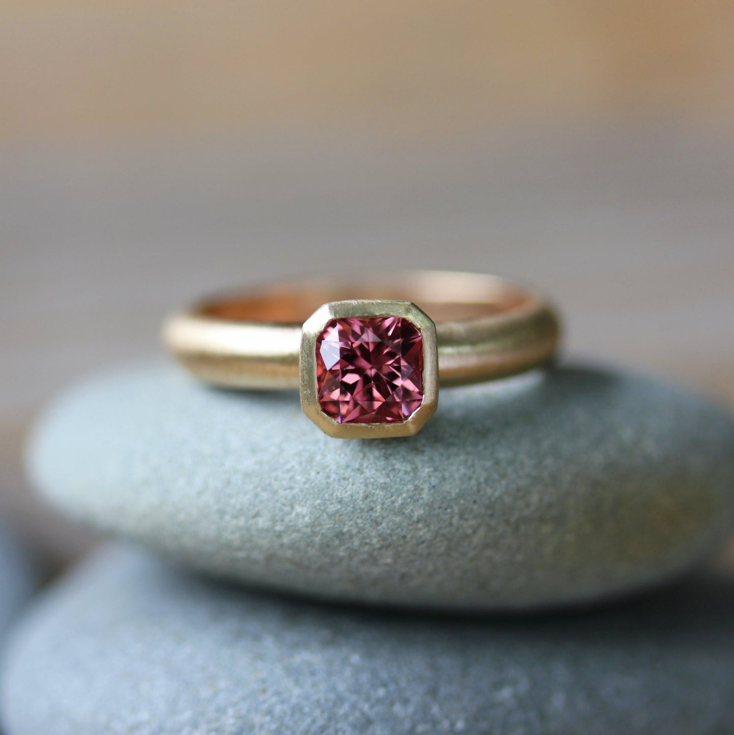 A Handmade Asscher Cut Pink Spinel Ring in 14k Yellow Gold with a pink sapphire on top of rocks.