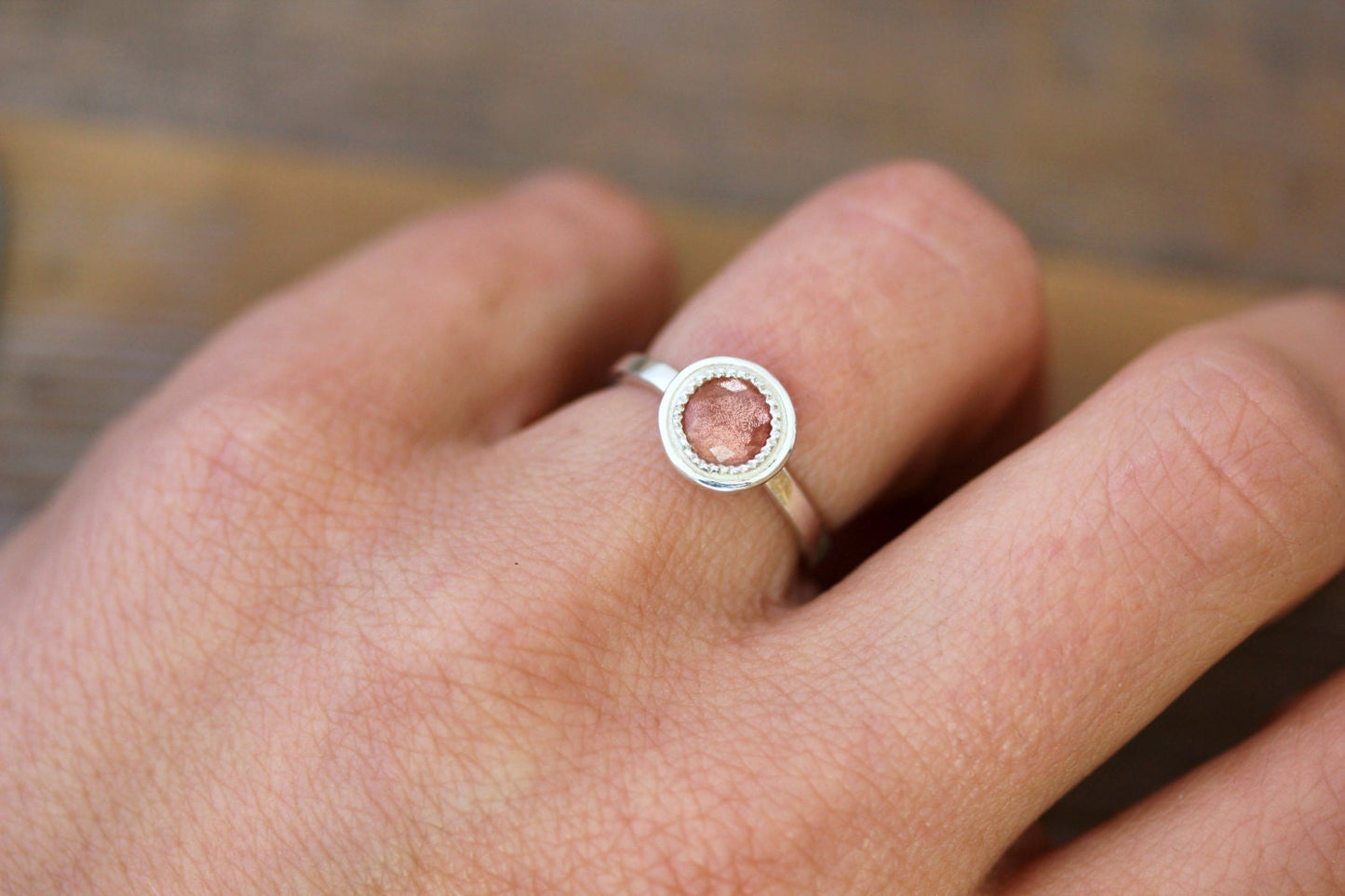 A woman's hand is holding a handmade Round Oregon Sunstone Ring in Sterling Silver with a pink stone.