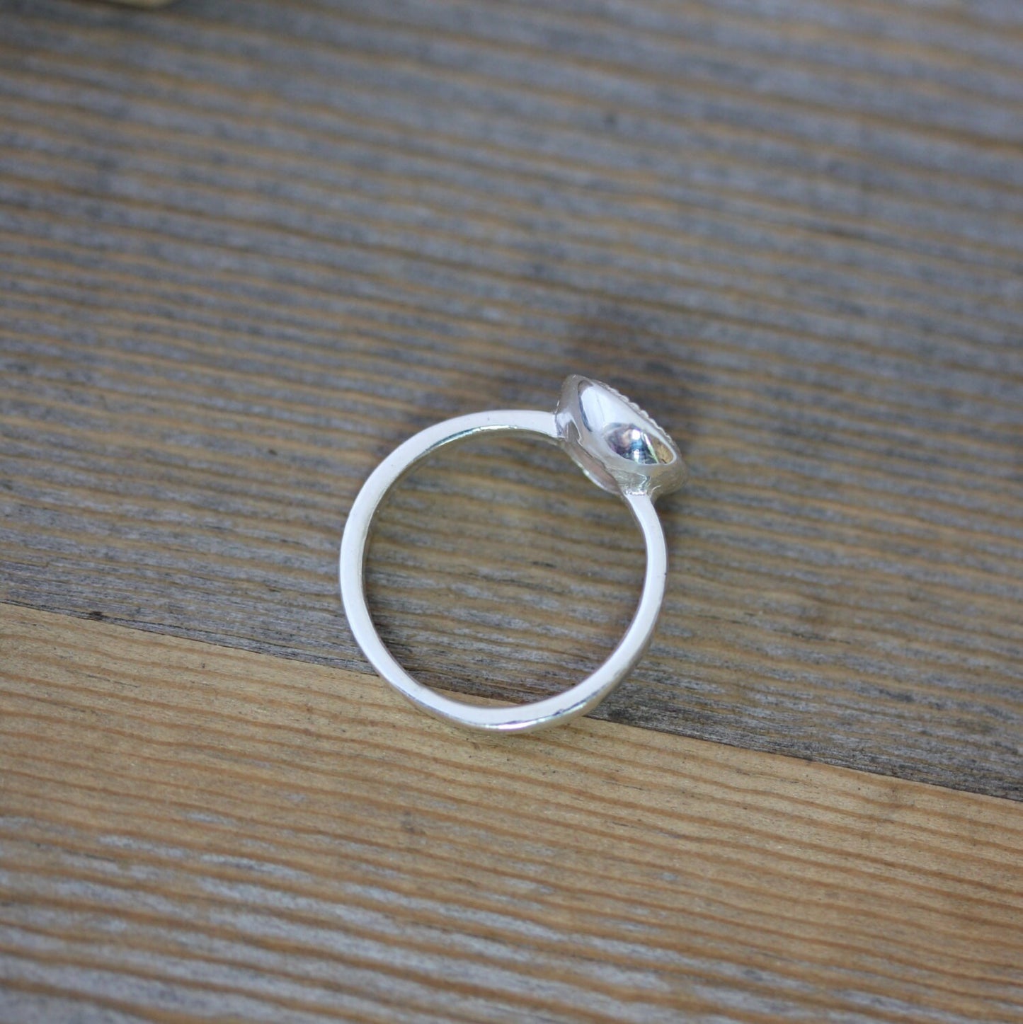 A handmade Oregon Sunstone ring in sterling silver on a wooden table.