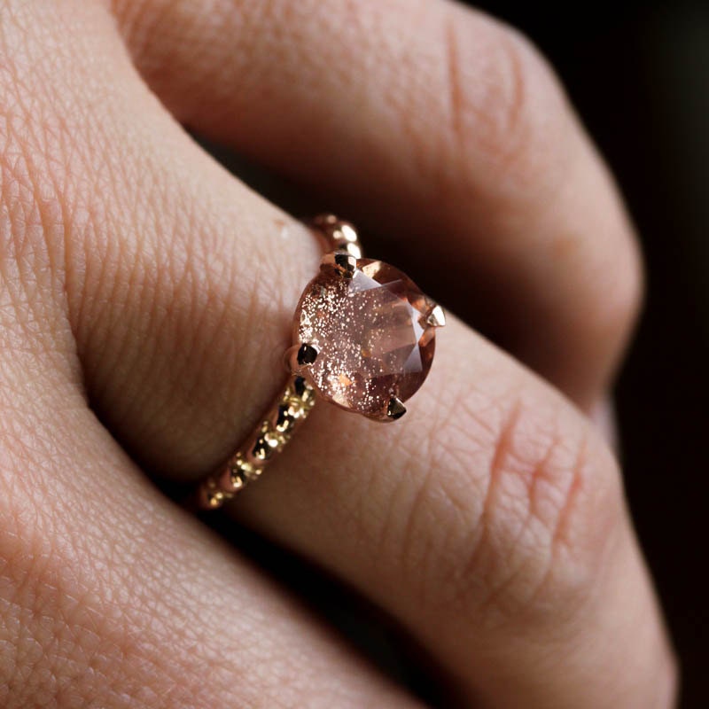 A woman's hand holding a Peachy Oregon Sunstone Ring in Rose Gold, handmade by Cassin Jewelry.