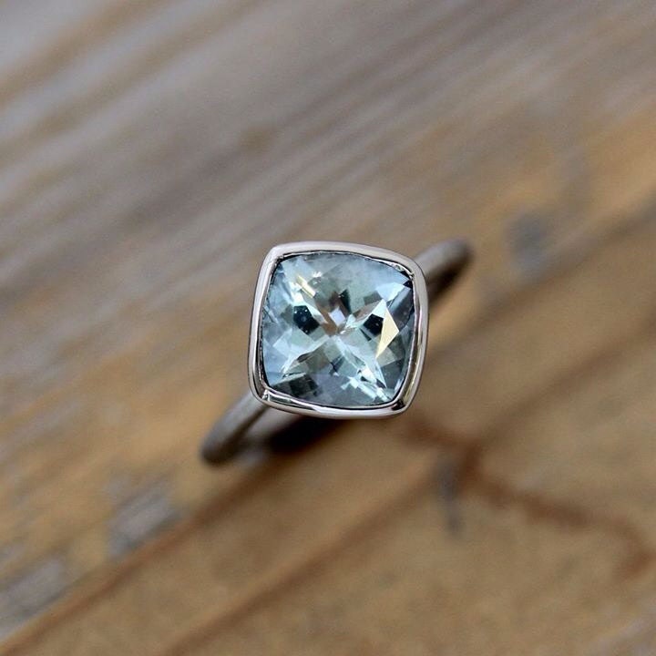A handmade cushion Aquamarine ring crafted by Cassin Jewelry, featuring a bezel-set blue gemstone for engagement.