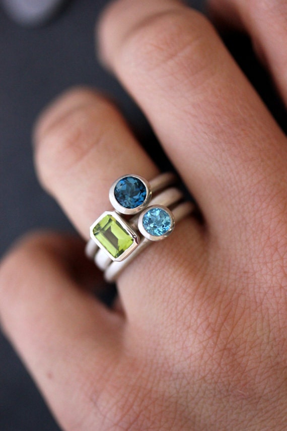A woman's hand is holding a Gemstone Stackable Rings in Emerald Cut Peridot, London Blue Topaz and Swiss Blue Topaz and Sterling Silver, Cassin handmade jewelry.