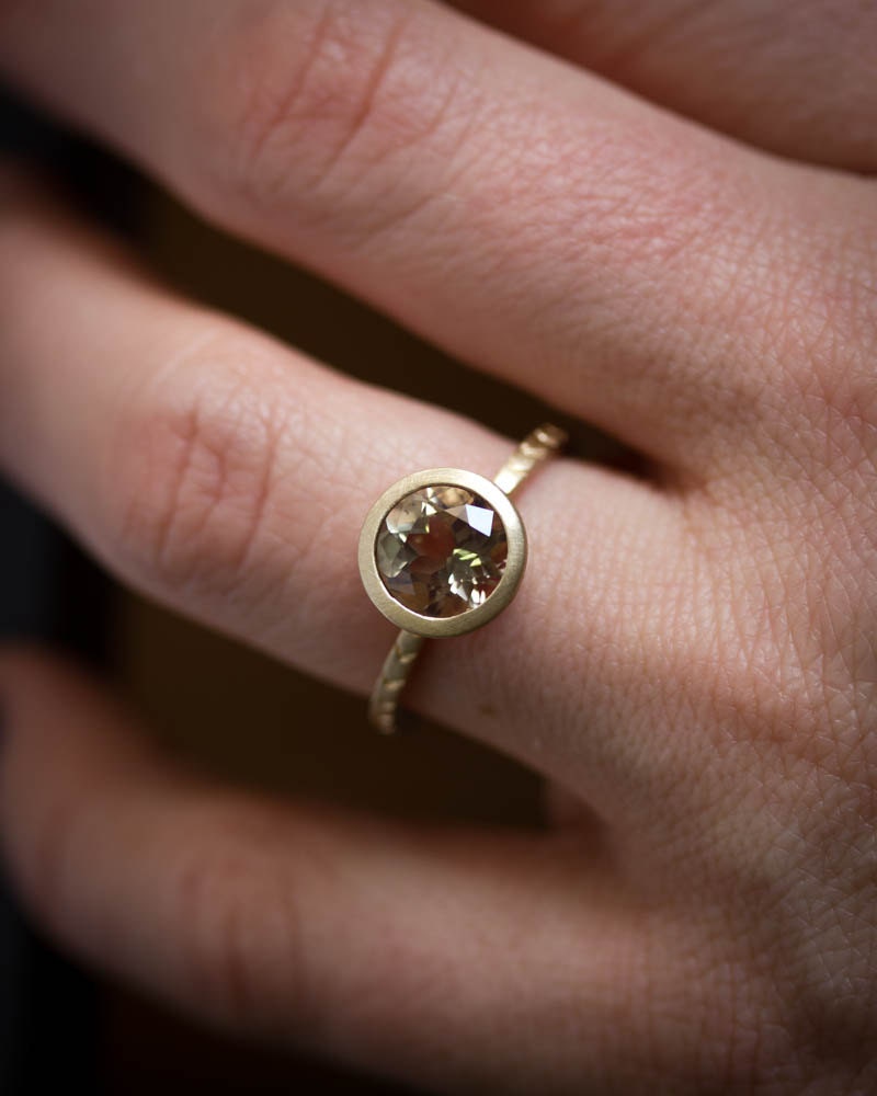 A woman's hand holding a Cassin handmade Oregon Sunstone Gold Ring with a brown diamond.