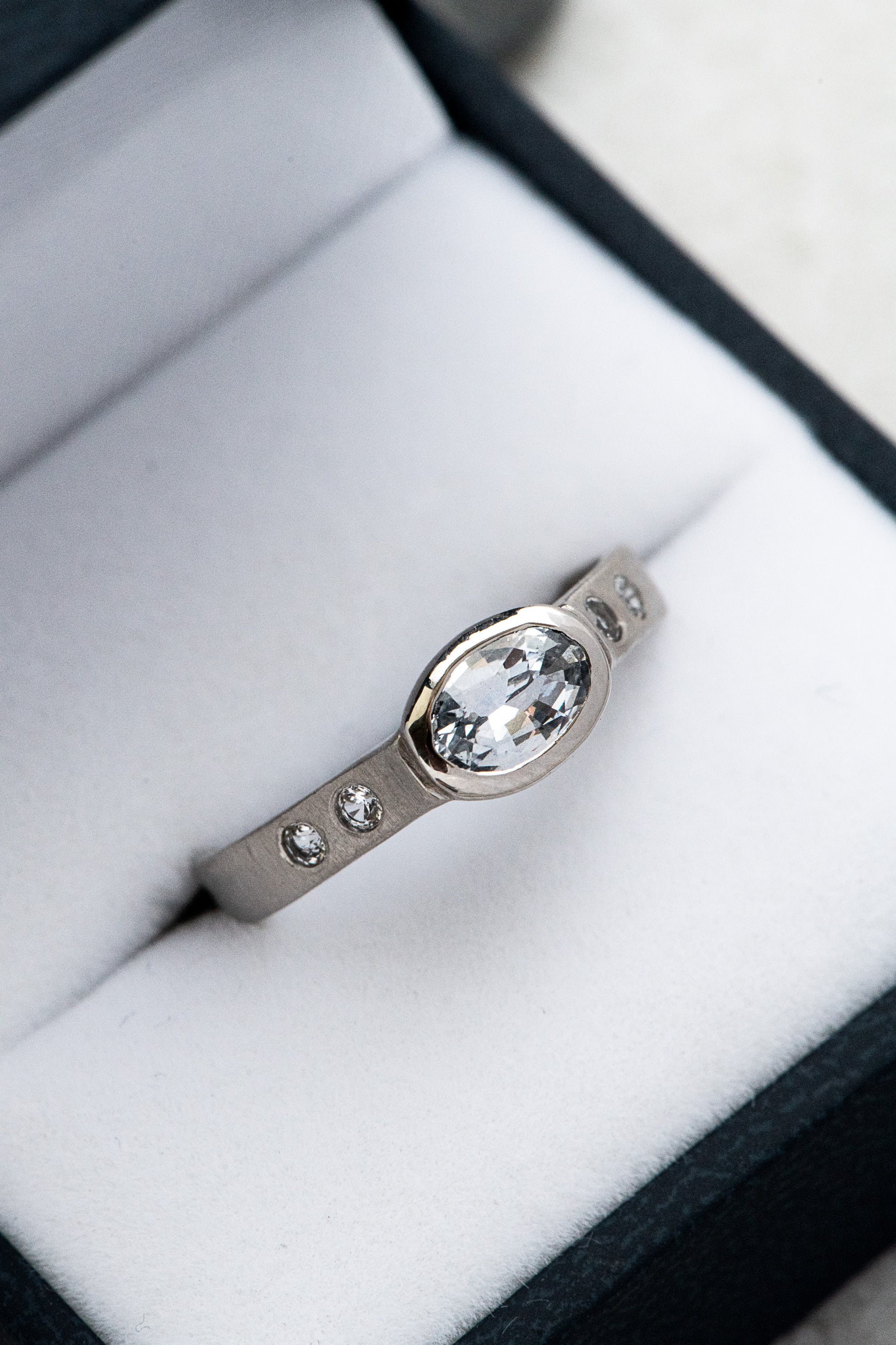 An oval Handmade White Sapphire Engagement Ring in a box by Cassin Jewelry.